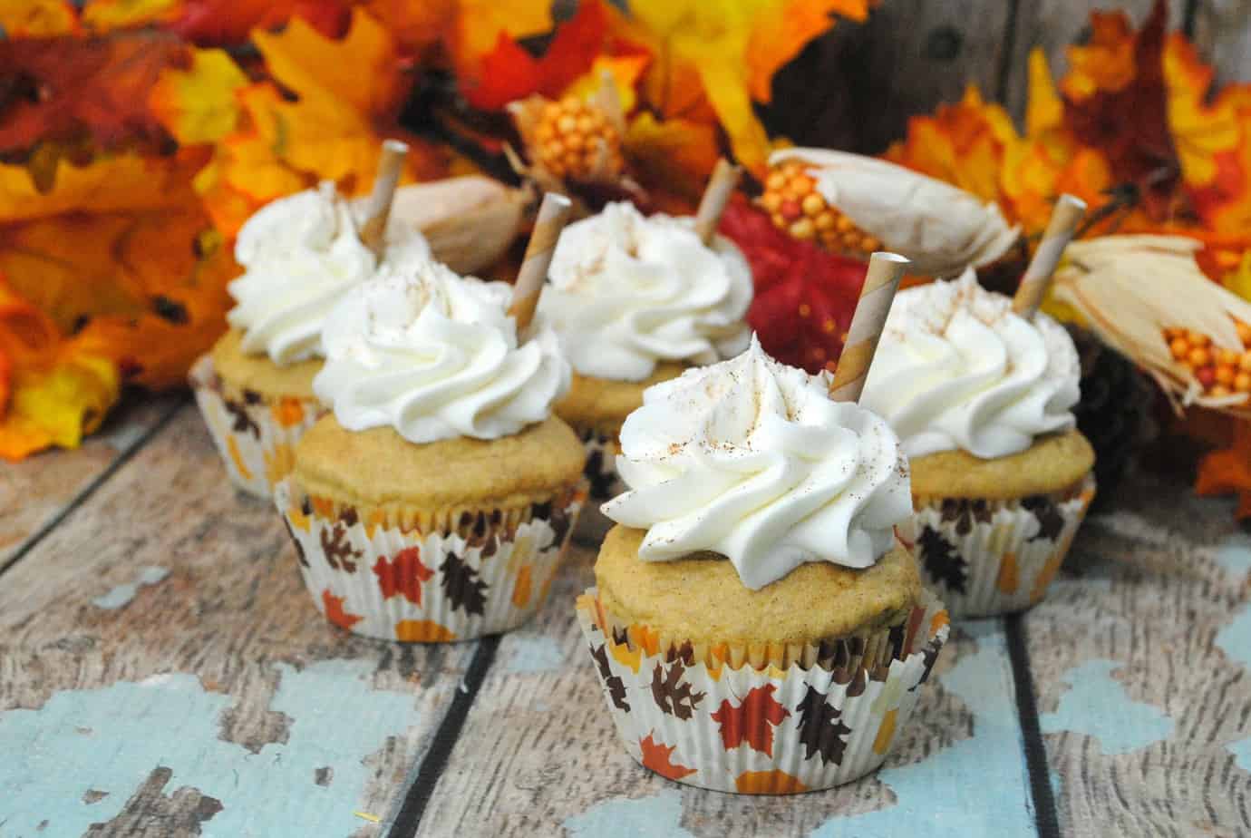 pumpkin spice latte cupcakes on a wood table with fake leaves in the background