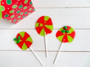 red and green jolly rancher suckers with a candy holly leaf at the top on a white table with a present in the background