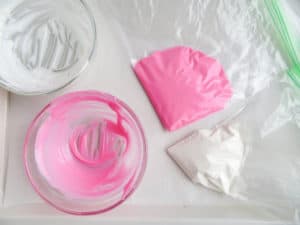 two plastic bags of pink and white melted candy next to two empty glass bowls with remnants of the melted candy on a white background