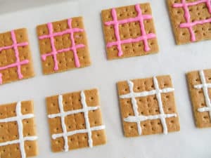 graham crackers with pink or white icing lines on them to look like a tic tac toe board on a white background