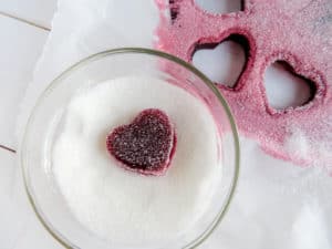 a heart gummy in a glass bowl of sugar next to a cut-out of the heart gummy