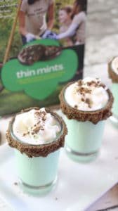 two thin mint shots in shot glasses rimmed with chocolate on a white plate on a wood table with a box of thin mints cookies in the background 