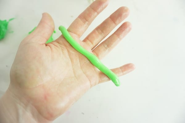 hand holding a rolled thin cylinder of green marshmallow fondant