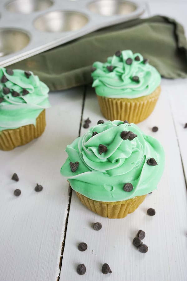 three boozy andes mint cupcakes with chocolate chips and green linen in the background on a white table