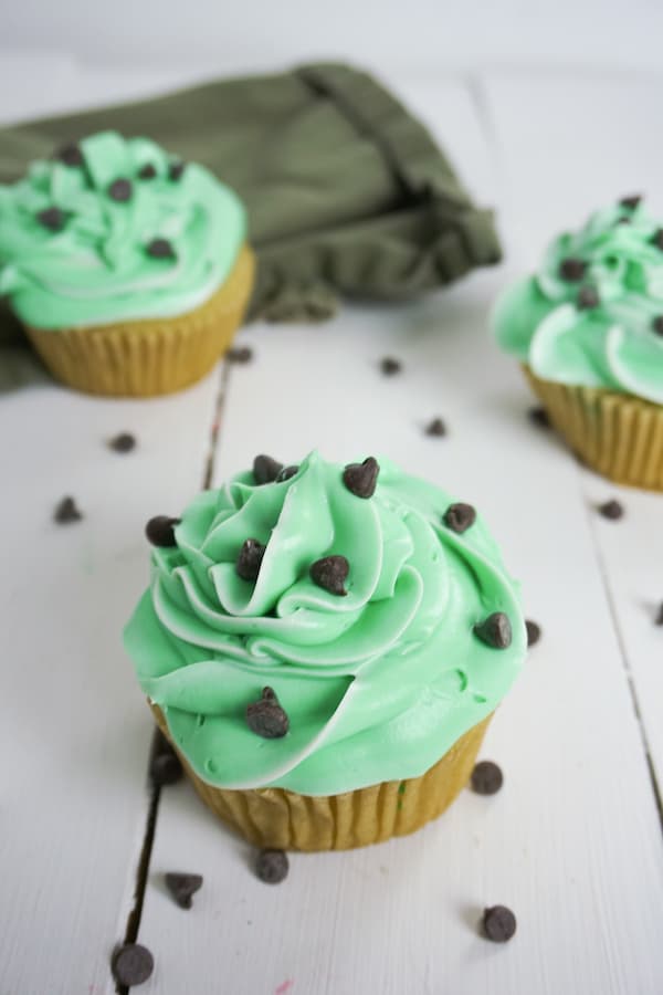 overhead view of three boozy andes mint cupcakes with chocolate chips on a white table and a green linen in the background