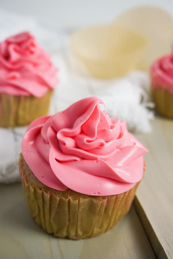 side view of three strawberry drunk cupcakes on a grey wood table with a white linen in the background