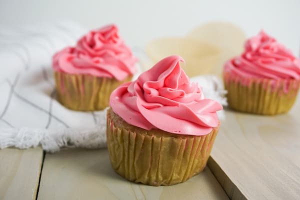 side view of three boozy strawberry cupcakes on a grey wood table with a white linen in the background