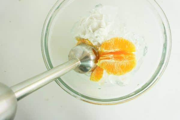 an immersion blender mixing the ingredients for an orange creamsicle margarita in a glass on a white table
