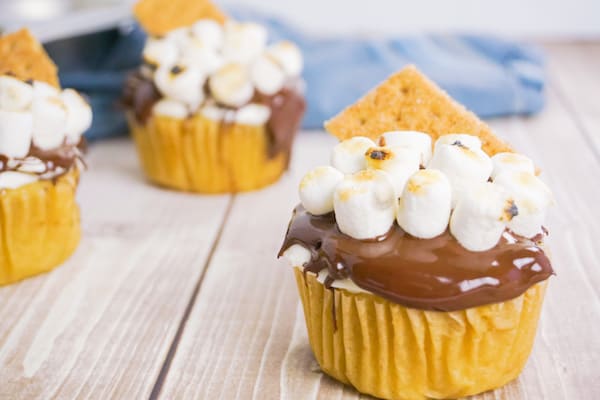 side view of three smores cupcakes on a wood table with a blue linen in the background