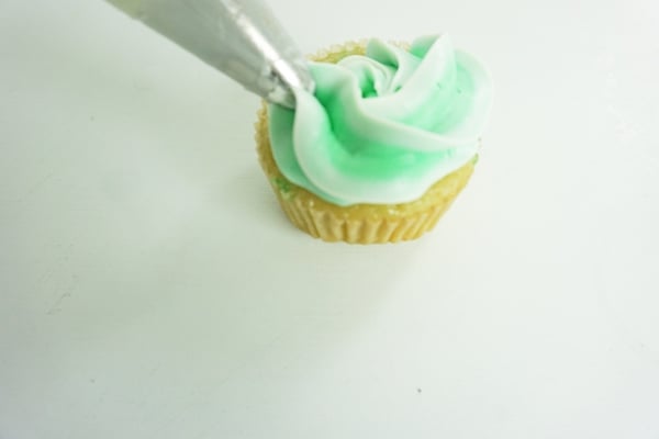 piping tip placing green icing on top of a cupcake on a white table