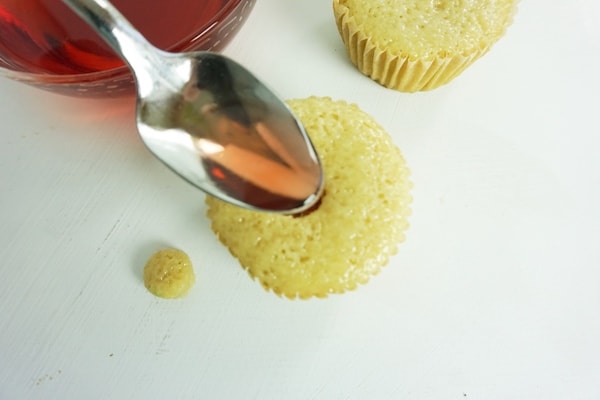spoon filling a cupcake well with strawberry liqueur mixture on a white table with another cupcake and bowl of strawberry liqueur in the background