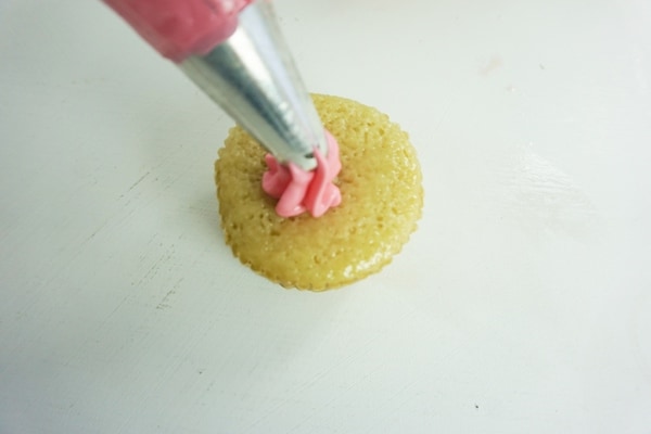 piping bag placing pink icing on a cupcake on a white table