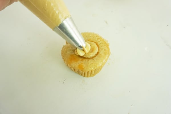 caramel frosting being piped into the middle of a cupcake on a white table