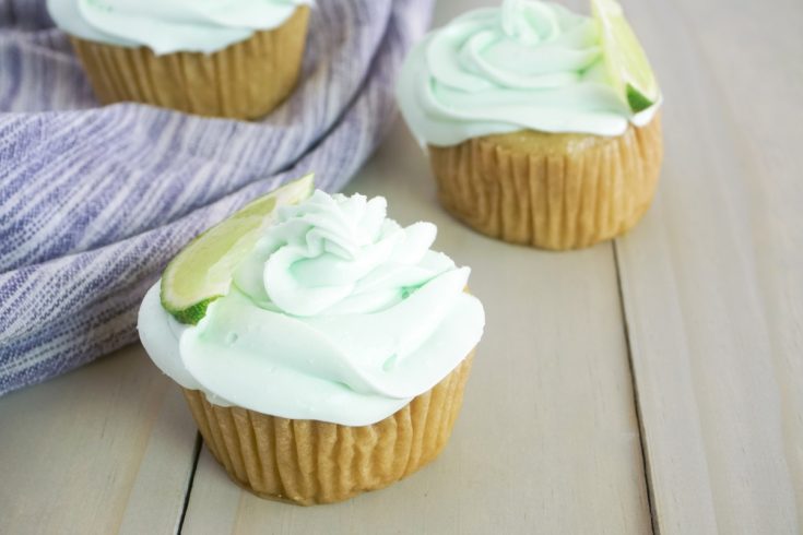 three margarita flavored cupcakes sitting on a grey wood table with a striped linen