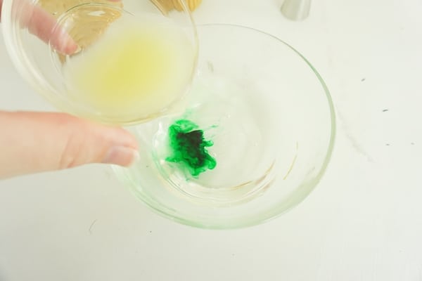 lime juice being added to a glass bowl of tequila and food coloring on a white table