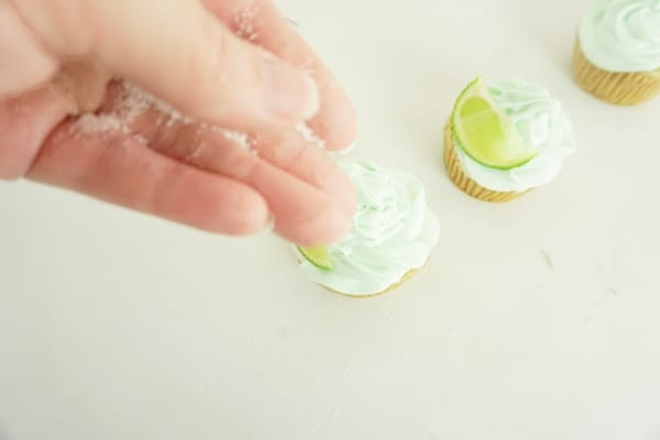 hand sprinkling salt onto margarita cupcakes on a white table