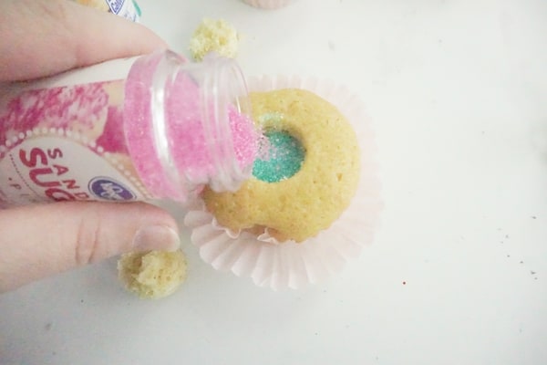 pink sanding sugar being poured into a hole in a cupcake with blue sanding sugar