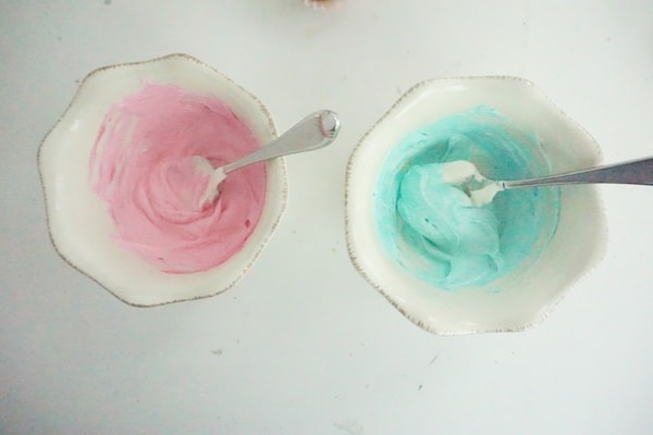 two bowls, one with pink icing and one with blue icing on a white table