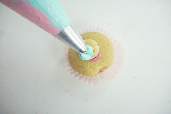 pink and blue icing being piped onto a cupcake