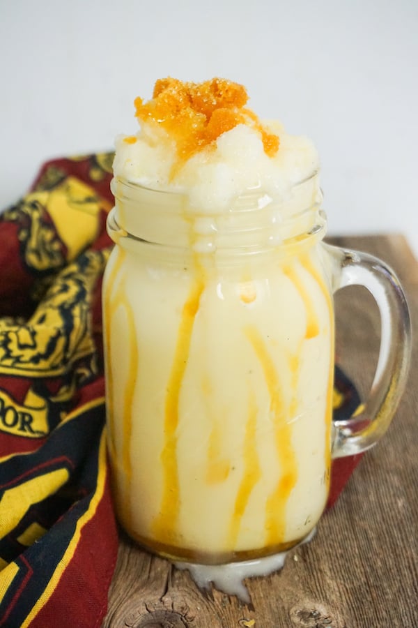 frappuccino with butterbeer flavoring in a glass mug on a wood background with gryffindor linen