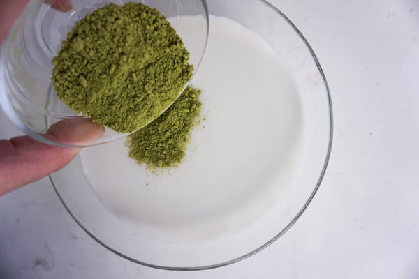 mixing matcha green tea in milk in a glass bowl on a white table