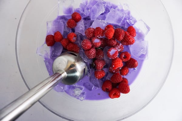 raspberries being blended with ice and purple-colored milk with an immersion blender to make a dragon frappucino