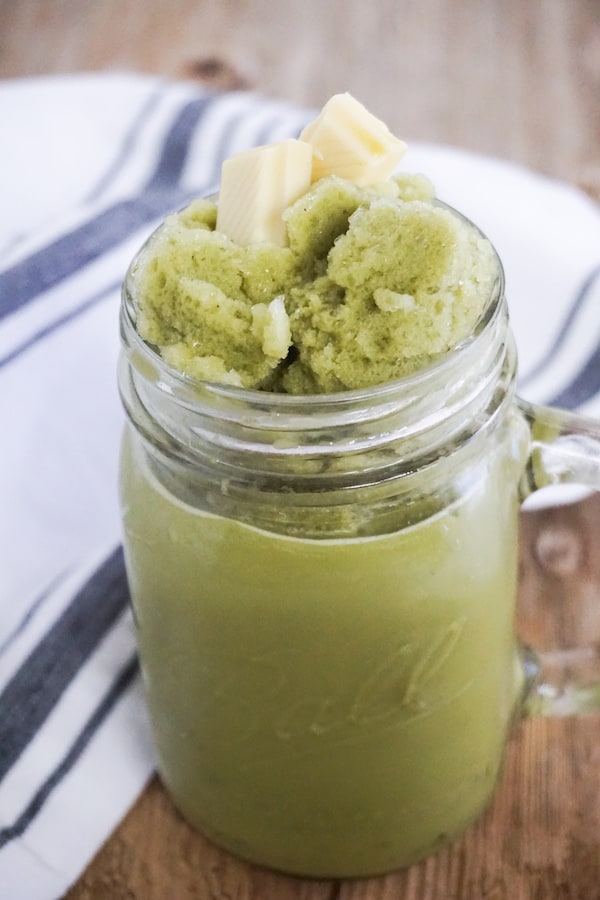 green tea matcha frappuccino in a glass jar mug on a wood table with a blue and white linen next to it
