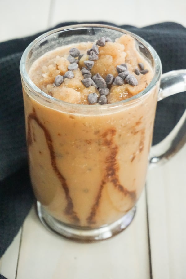 close-up view of a chocolate flavored frappuccino in a glass mug topped with chocolate chips on a grey wood background with black linen