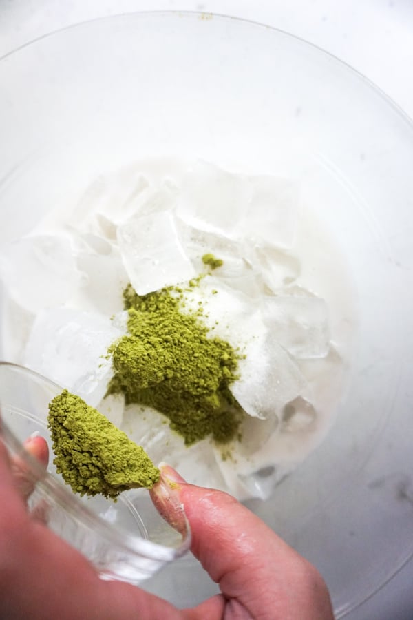 machta green tea powder being added to a bowl of ice and milk to make a mermaid frappuccino