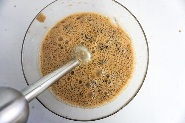 mocha frappuccino being blended in a glass bowl with an immersion blender on a white table
