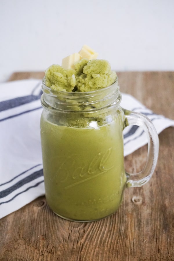 green tea matcha frappuccino in a glass jar mug on a wood table with a blue and white linen next to it