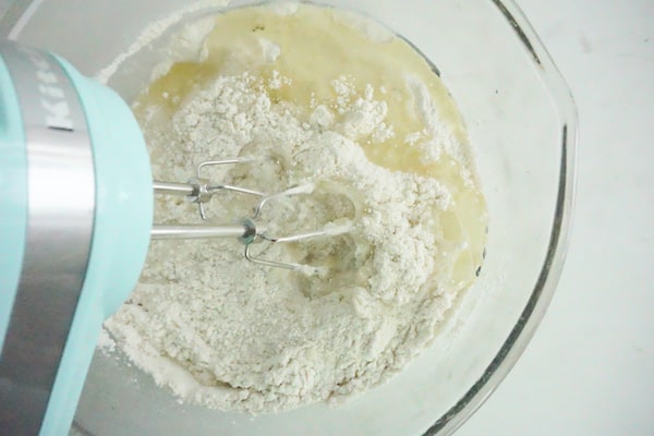 a green kitchen aid mixer, mixing the cupcake batter ingredients in a glass mixing bowl on a white counter
