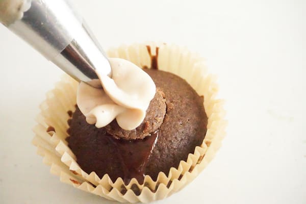 a cupcake being frosted with a pastry bag and decorating tip