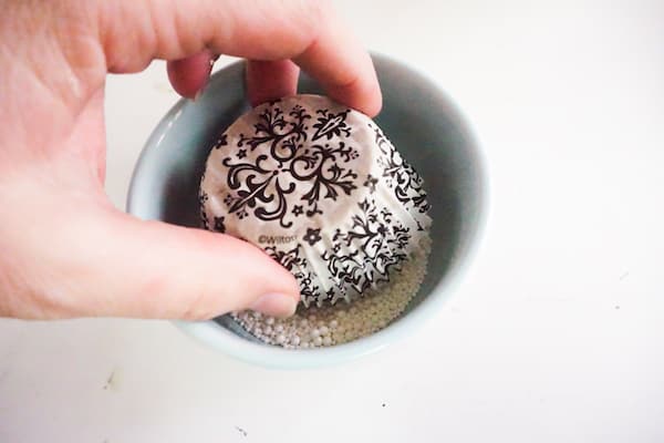 a hand dipping a cupcake into a bowl of white pearl sprinkles on a white counter