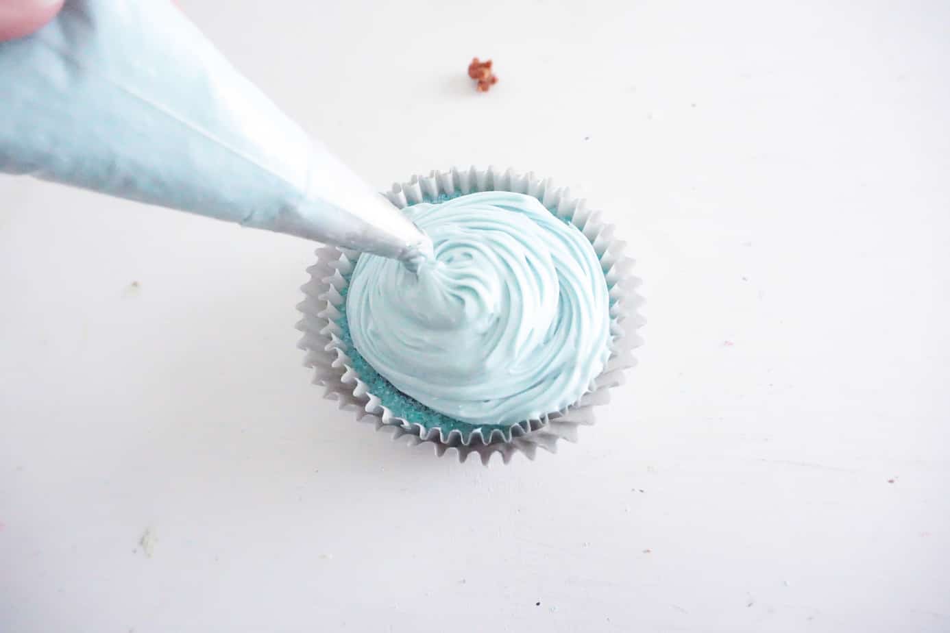 a pastry bag being used to put blue frosting on a cupcake on a white counter
