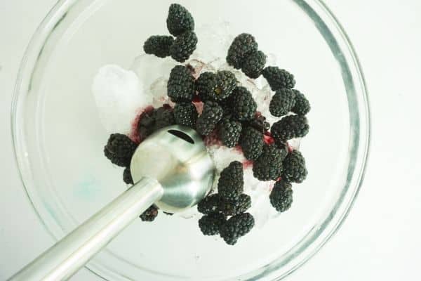 bowl of ice and blackberries being blended with an immersion blender