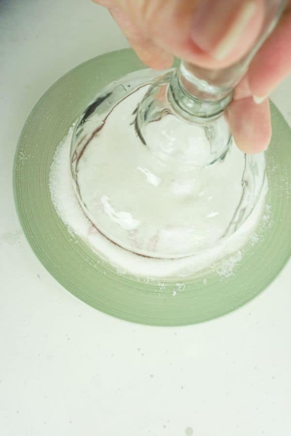 upside down margarita glass being placed in sugar on a green plate with a white background