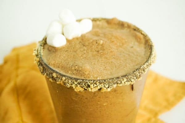closeup of s'mores margarita in glass on orange dish towel, glass rimmed with chocolate and graham cracker crumbs, drink garnished with mini marshmallows
