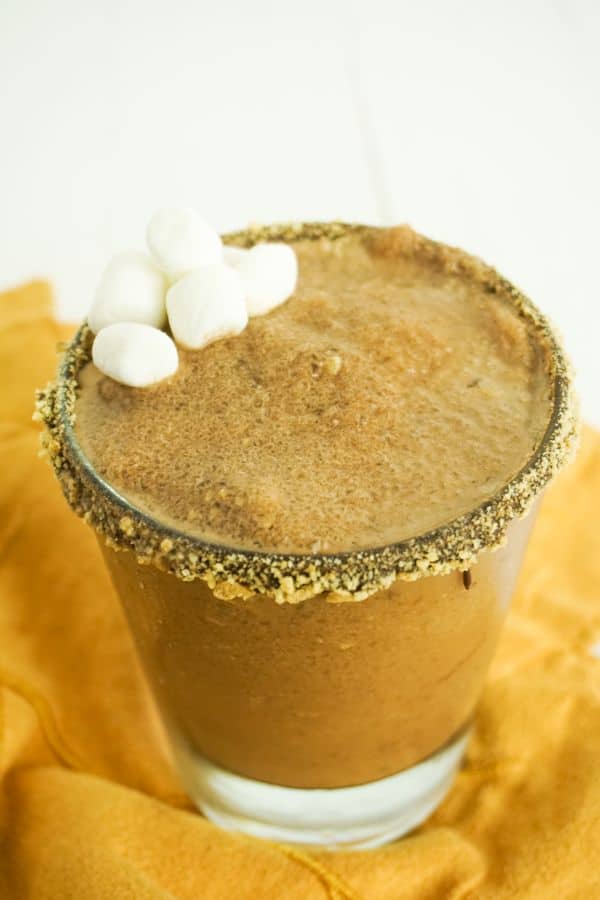 closeup of s'mores margarita in glass on orange dish towel, glass rimmed with chocolate and graham cracker crumbs, drink garnished with mini marshmallows