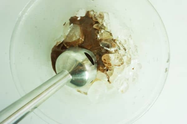 an immersion blender in a glass bowl mixing up melted chocolate, ice and triple sec