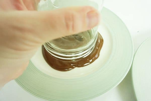 a hand holding a glass upside down in a plate of melted chocolate