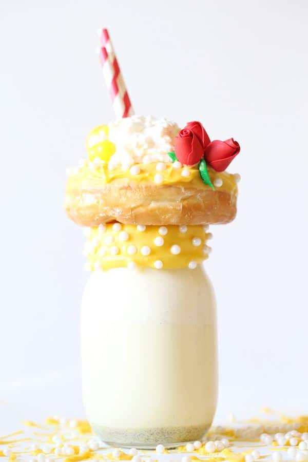 beauty and the beast freak shake in a glass topped with a yellow frosted donut and red fondant in the shape of roses on a white background