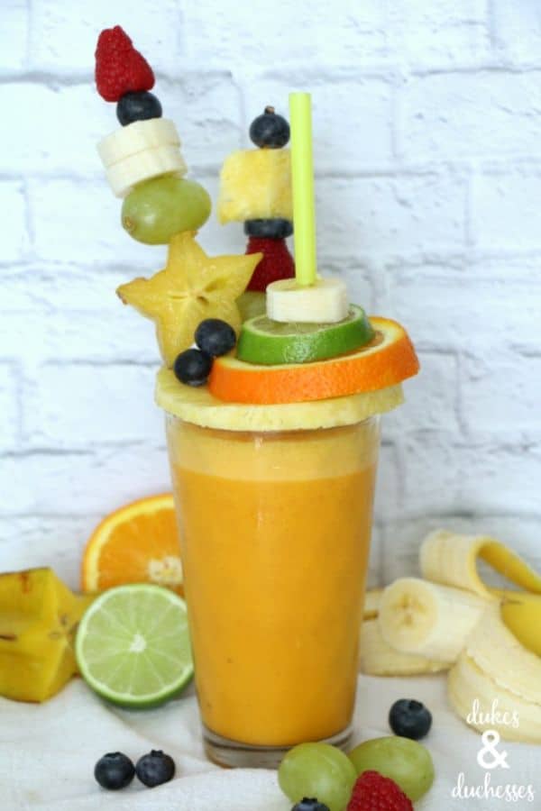 freakshake extreme smoothie in a glass topped with fruit slices and skewers with a white brick background