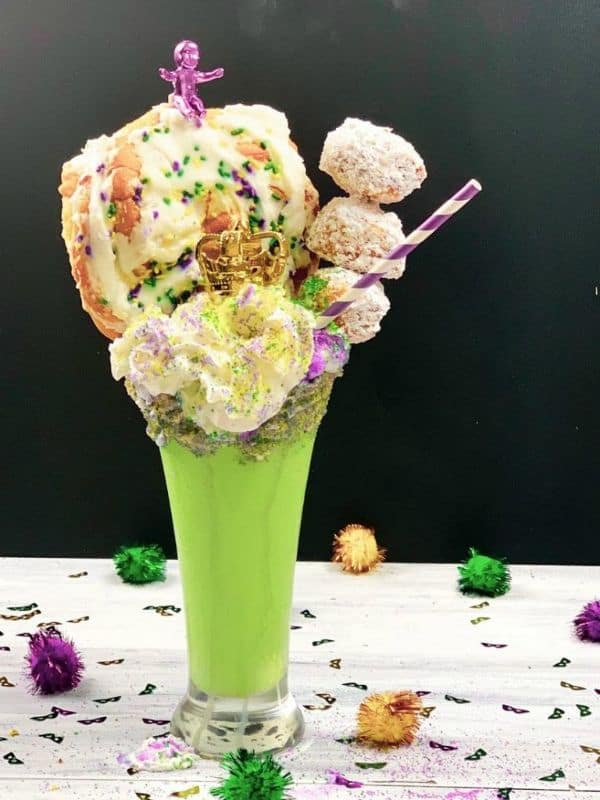 mardi gras milkshake in a glass topped with whipped cream and mini donuts on a black background