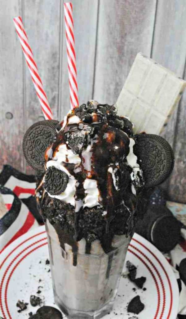 oreo freak shake in a glass topped with oreos, whipped cream and chocolate sauce on a white plate with a wood background