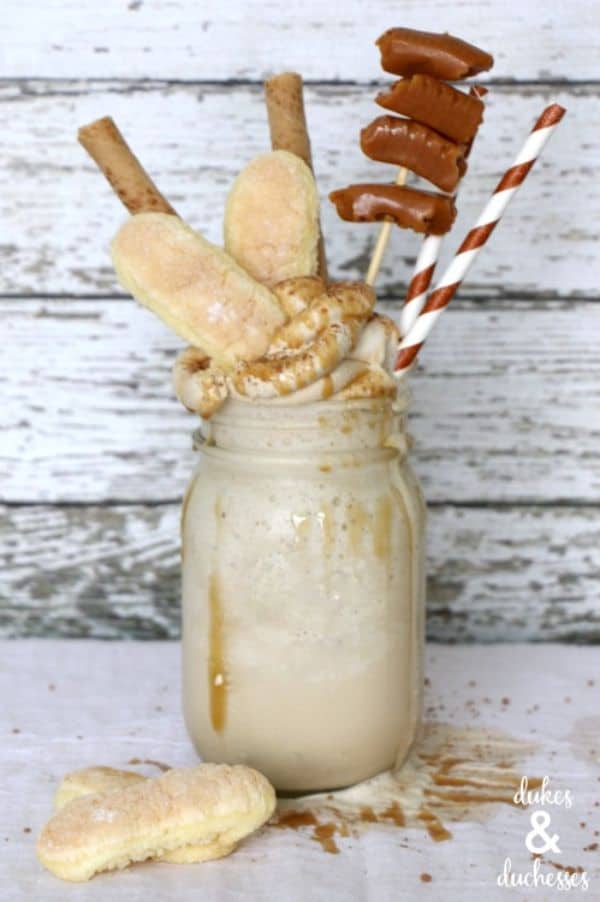 tiramisu cold brew freakshake in a glass topped with whipped cream, cookies, and tootsie rolls on a wood background