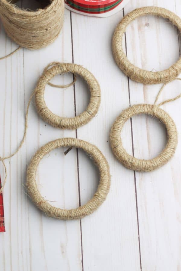 mason jar lid rings wrapped in twine next to a ball of twine and a roll of red and green ribbon on a white wood table