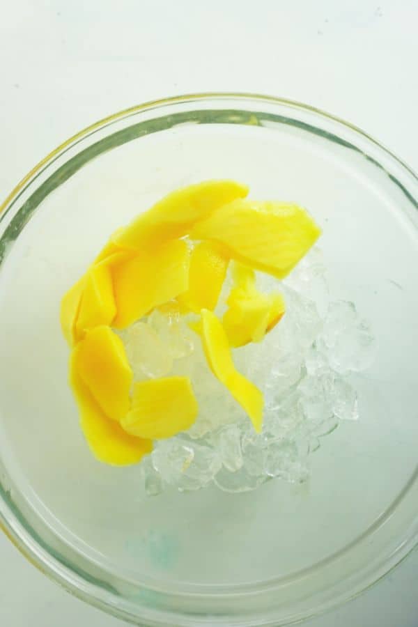 mango pieces and ice in a glass bowl on a white background