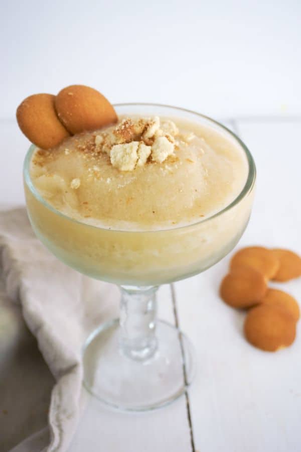 Banana Pudding Margarita in a glass next to a brown cloth and vanilla wafers on a white table