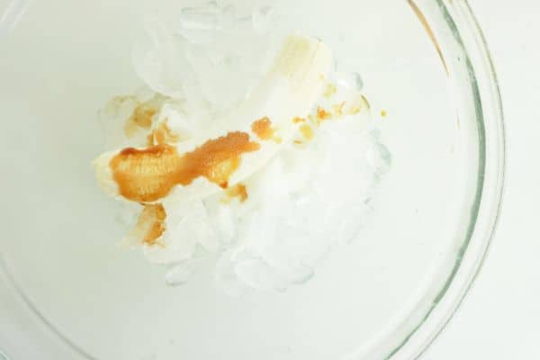ice, banana, and vanilla extract in a glass bowl on a white background